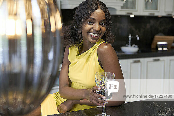 Portrait of happy young woman with glass of red wine sitting in the kitchen