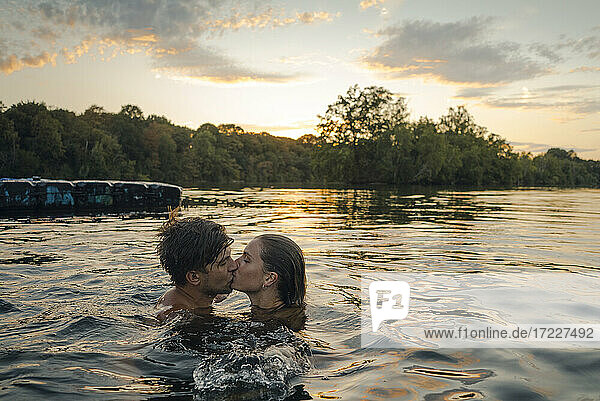 Junges Paar schwimmt im See und küsst sich bei Sonnenuntergang