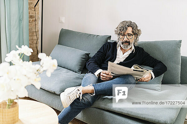 Älterer Mann liest Zeitung  während er zu Hause auf dem Sofa sitzt