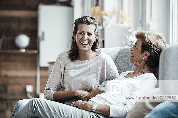 Laughing woman sitting by grandmother on sofa at home