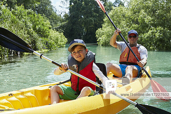 Smiling boy looking away while canoeing with father in lake