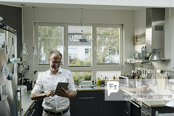 Älterer Mann  der ein digitales Tablet benutzt  während er in der Küche zu Hause steht