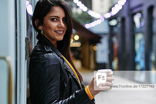 Beautiful woman standing with disposable coffee cup in city