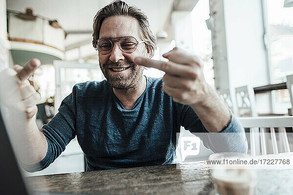 Happy male entrepreneur showing obscene gesture at cafe