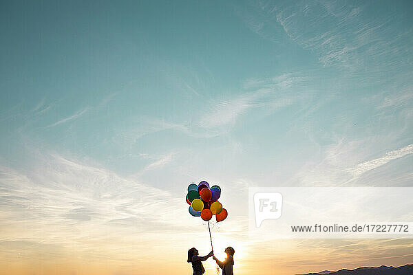 Mädchen in Silhouette spielen mit bunten Luftballons bei Sonnenuntergang