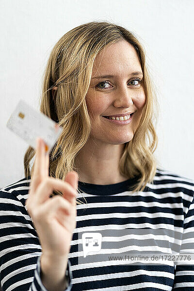 Lächelnde blonde Frau hält Kreditkarte zu Hause