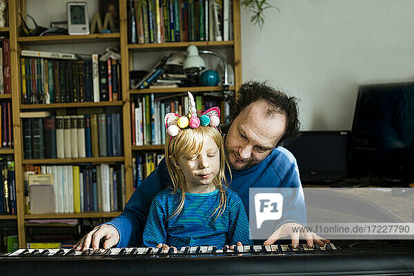 Mann bringt seiner Tochter zu Hause sitzend Synthesizer bei