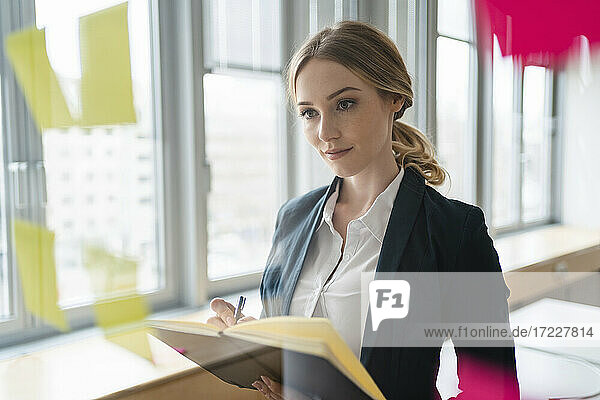 Female professional planning business strategy while writing in diary at office