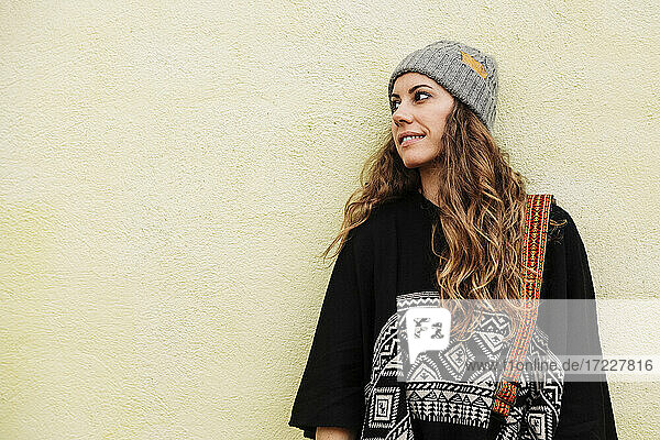 Lächelnde Frau mit braunen Haaren  die nachdenklich vor einer Wand steht