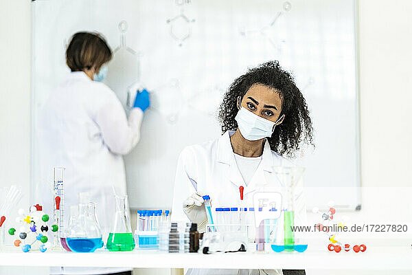 Forscherin bei der Arbeit  während ein Kollege im Labor auf einer Tafel zeichnet