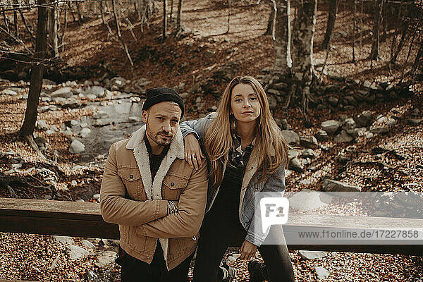 Hipster-Mann steht neben seiner Freundin  die auf einem Holzgeländer im Wald sitzt  im Herbst