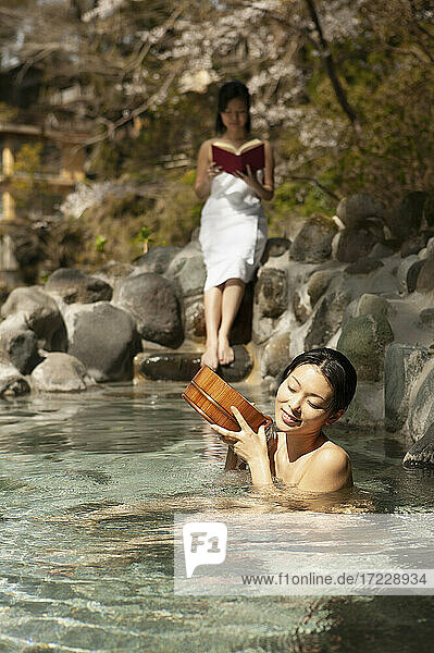 Junge Frauen entspannen und lesen am sonnigen Onsen-Pool