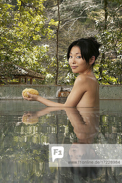 Porträt schöne nackte junge Frau mit Luffa im Pool bei Onsen