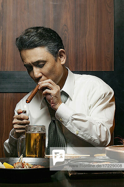 Businessman lighting cigar at restaurant table