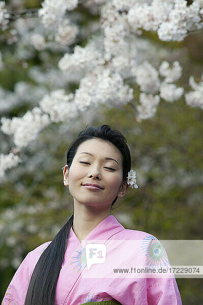 Schöne heitere junge Frau im Kimono unter Kirschblüten