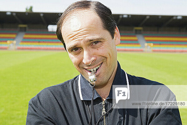 Portrait smiling confident male soccer coach with whistle on field