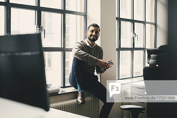 Porträt von lächelnden Geschäftsmann mit Box sitzen gegen Fenster in kreativen Büro