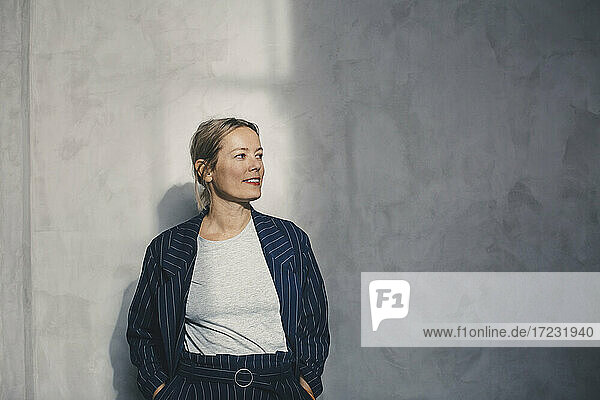 Female entrepreneur with hands in pockets looking away against gray wall