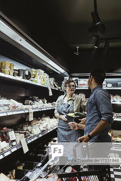 Female store owner talking with male customer at delicatessen shop
