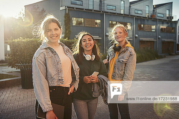 Porträt von lächelnden Freundinnen  die auf einem Fußweg vor einem Gebäude stehen