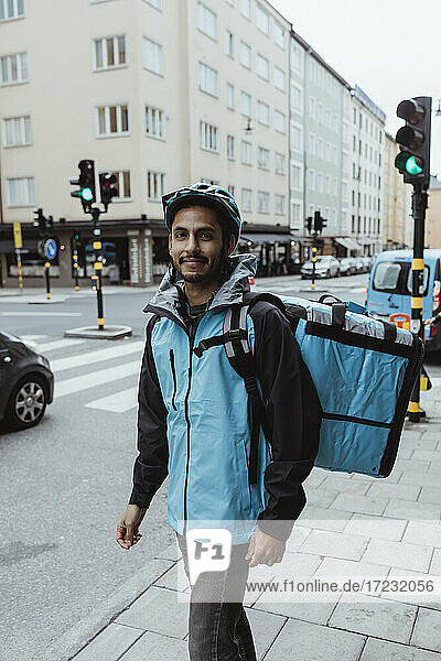 Porträt der lächelnden Lieferung Mann auf dem Bürgersteig in der Stadt stehen