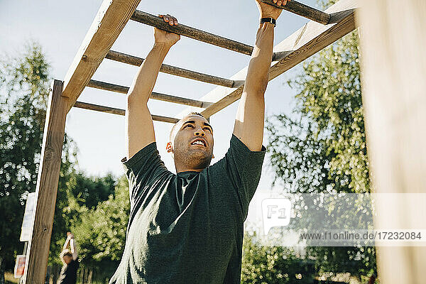 Männlicher Athlet hängt an der Affenstange im Park an einem sonnigen Tag