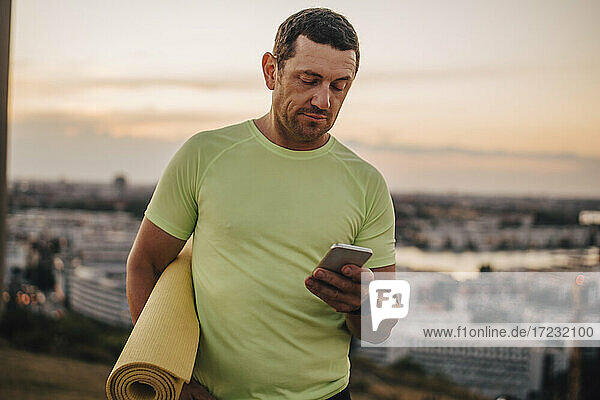 Älterer männlicher Sportler mit Handy gegen den Himmel bei Sonnenuntergang