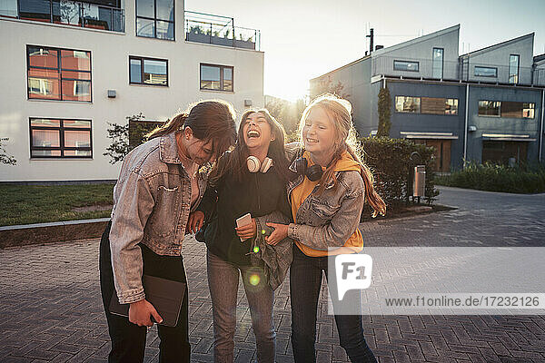 Fröhliche Freundinnen lachend auf Fußweg gegen Gebäude