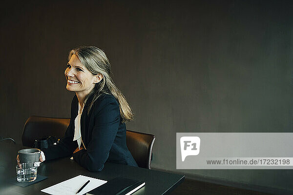 Lächelnde Geschäftsfrau schaut mit Kaffeetasse im Büro weg