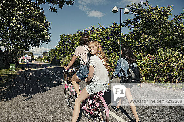 Teenager-Mädchen zu Fuß durch weibliche Freunde Radfahren auf der Straße während sonnigen Tag