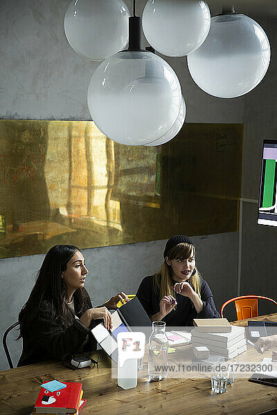 Glückliche weibliche Kollegen diskutieren über Produkt während der Sitzung im kreativen Büro