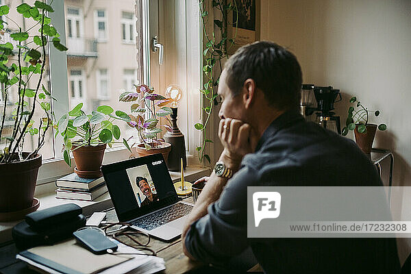 Male entrepreneur discussing with colleague on video call through laptop at home during COVID-19