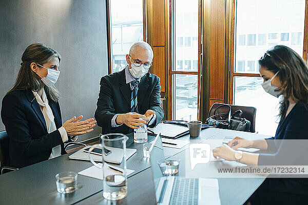 Männliche und weibliche Kollegen beim Auftragen von Desinfektionsmittel im Sitzungssaal des Büros während einer Pandemie
