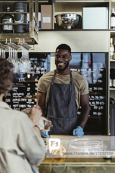 Smiling male entrepreneur looking at female customer in deli store