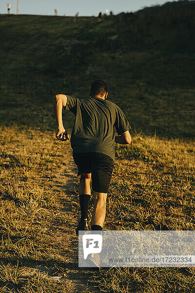 Rückansicht eines männlichen Sportlers  der bei Sonnenuntergang an Land läuft