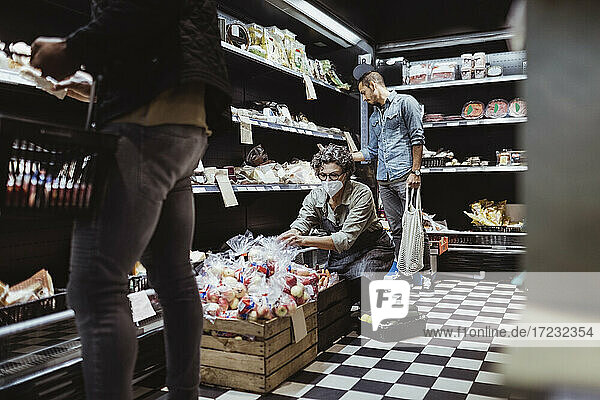 Male customer shopping while female owner crouching by in delicatessen store