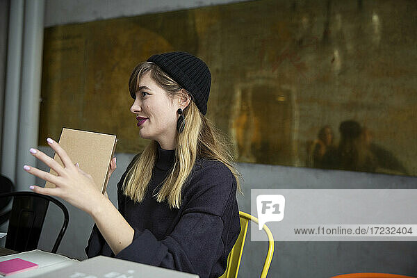 Lächelnde Geschäftsfrau mit Produkt-Box sitzen in kreativen Büro