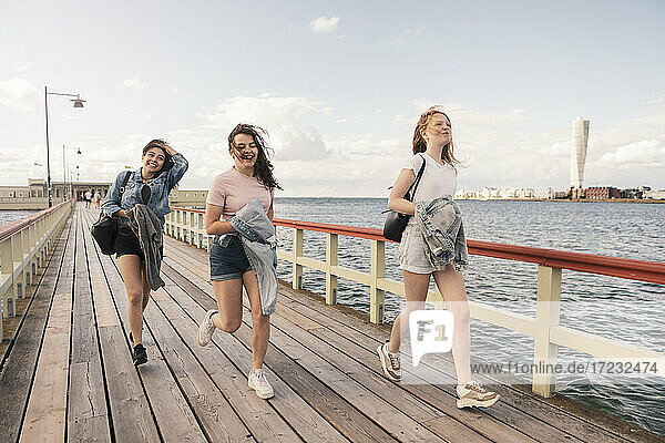 Weibliche Freunde laufen auf Pier am Meer gegen den Himmel