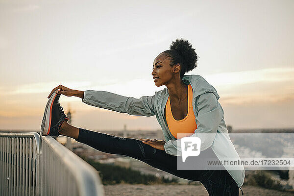 Sportlerin tun Stretching-Übung gegen den Himmel während des Sonnenuntergangs