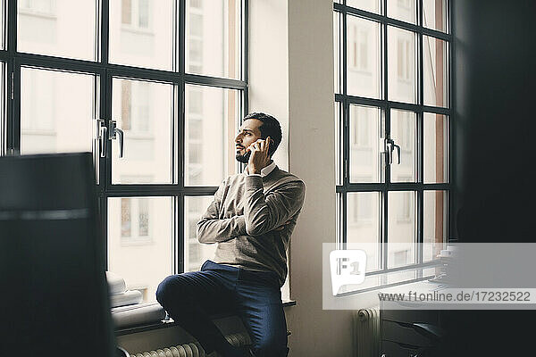 Male entrepreneur talking on smart phone by window in creative office