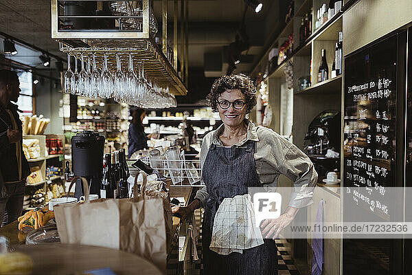 Porträt einer lächelnden Besitzerin mit Hand auf der Hüfte in einem Feinkostladen