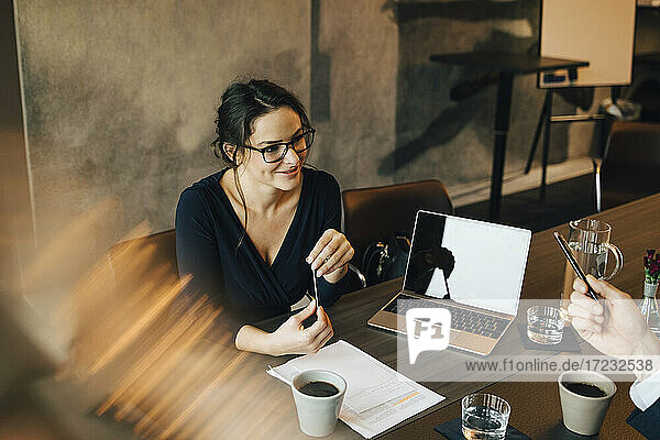 Lächelnde Geschäftsfrau im Gespräch mit Kollegen während einer Besprechung im Büro