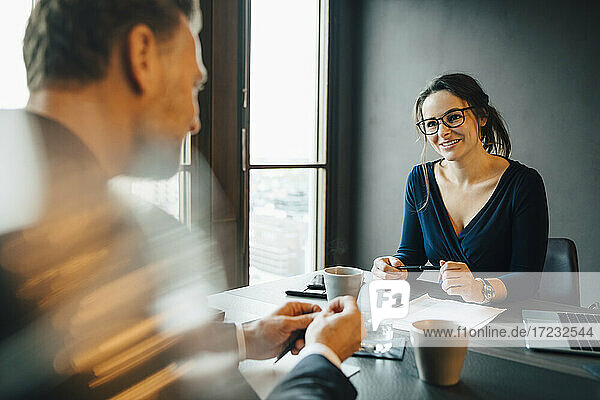 Lächelnde Geschäftsfrau  die mit einem männlichen Kollegen im Sitzungssaal im Büro diskutiert