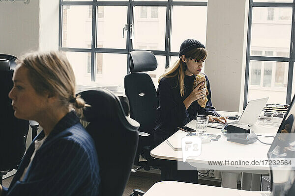 Geschäftsfrau essen Essen während der Arbeit am Laptop im Büro