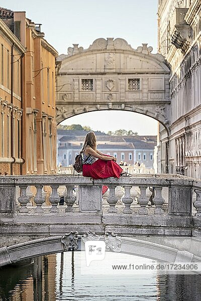 Junge Frau mit rotem Rock  Touristin sitzt auf einer Brückengeländer  Brücke über dem Rio di Palazzo  hinten Seufzerbrücke  Venedig  Venetien  Italien  Europa
