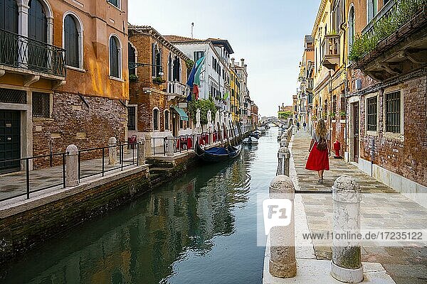Junge Frau mit rotem Rock geht zwischen Kanal und alten Häusern  Venedig  Venetien  Italien  Europa