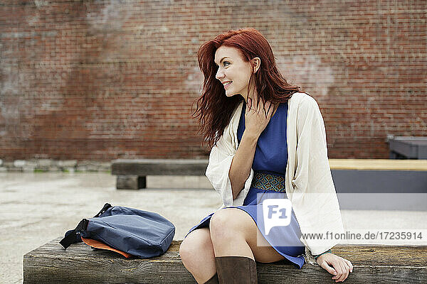 Junge Frau mit langen roten Haaren  auf Bank sitzend  wegschauend
