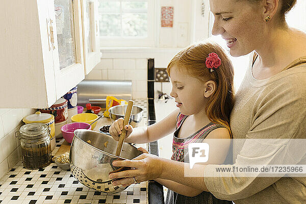 Mädchen und Mutter mischen Zutaten in einer Schüssel in der Küche