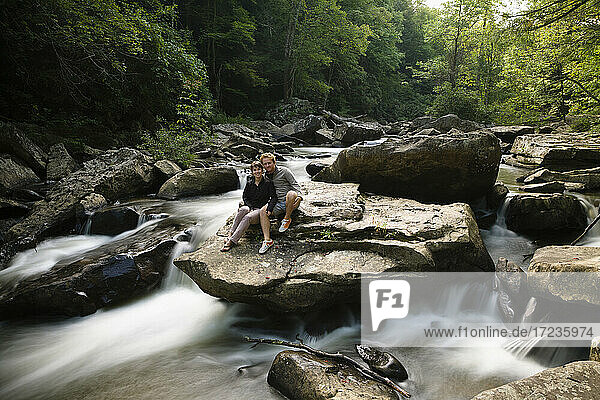 Porträt eines mittleren erwachsenen Paares  zusammen auf einem Felsen im Wasserfall sitzend  New River Gorge National River  Fayetteville  West Virginia  USA