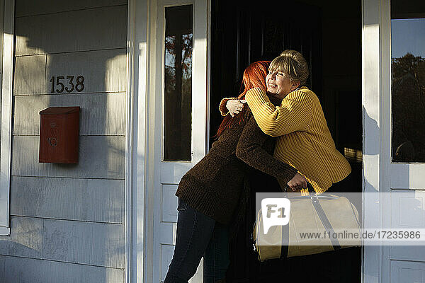 Ältere Frau und erwachsene Tochter umarmen sich an der Haustür
